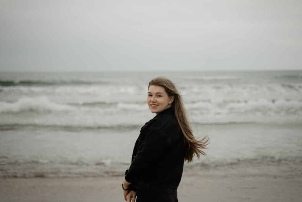 young girl smiling while standing on the beach, hair fluttering